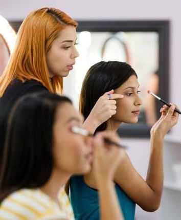 Women applying makeup with brushes in a beauty class.