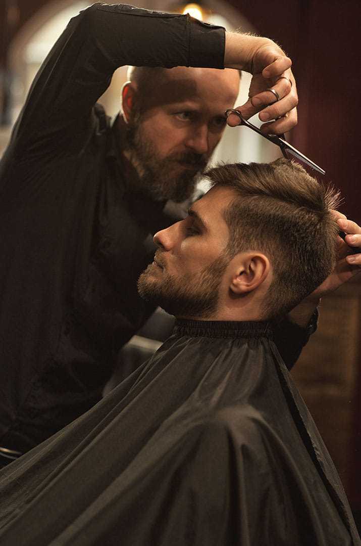 Barber trimming a man's hair with scissors in a salon.