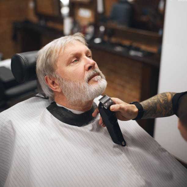 Man in barber chair getting beard trimmed with an electric trimmer.