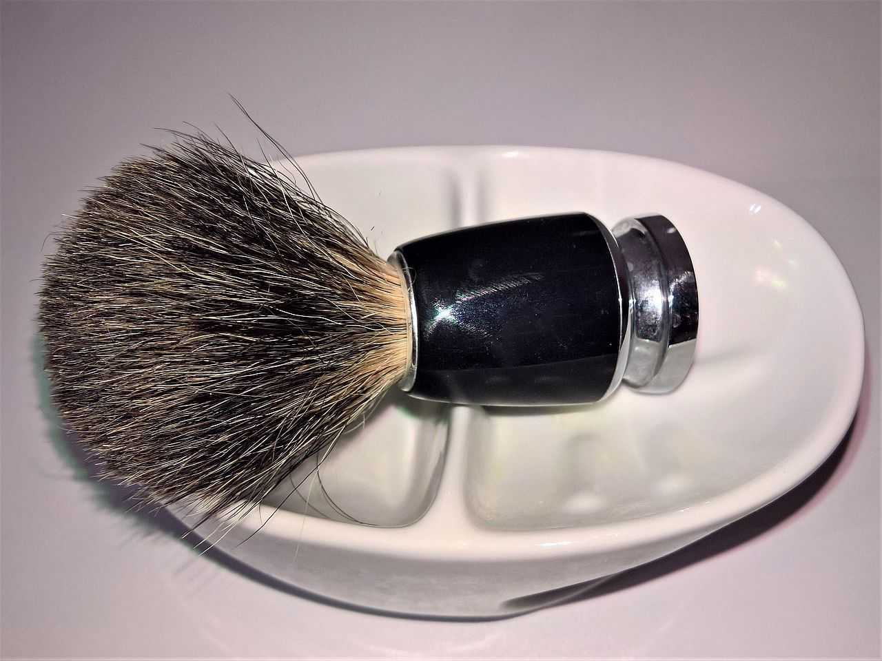 Shaving brush with black handle resting in a white porcelain bowl.