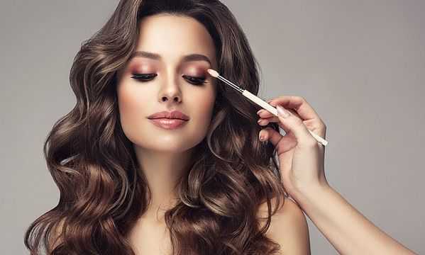 Woman getting eye makeup applied with a brush, showcasing a glam look.