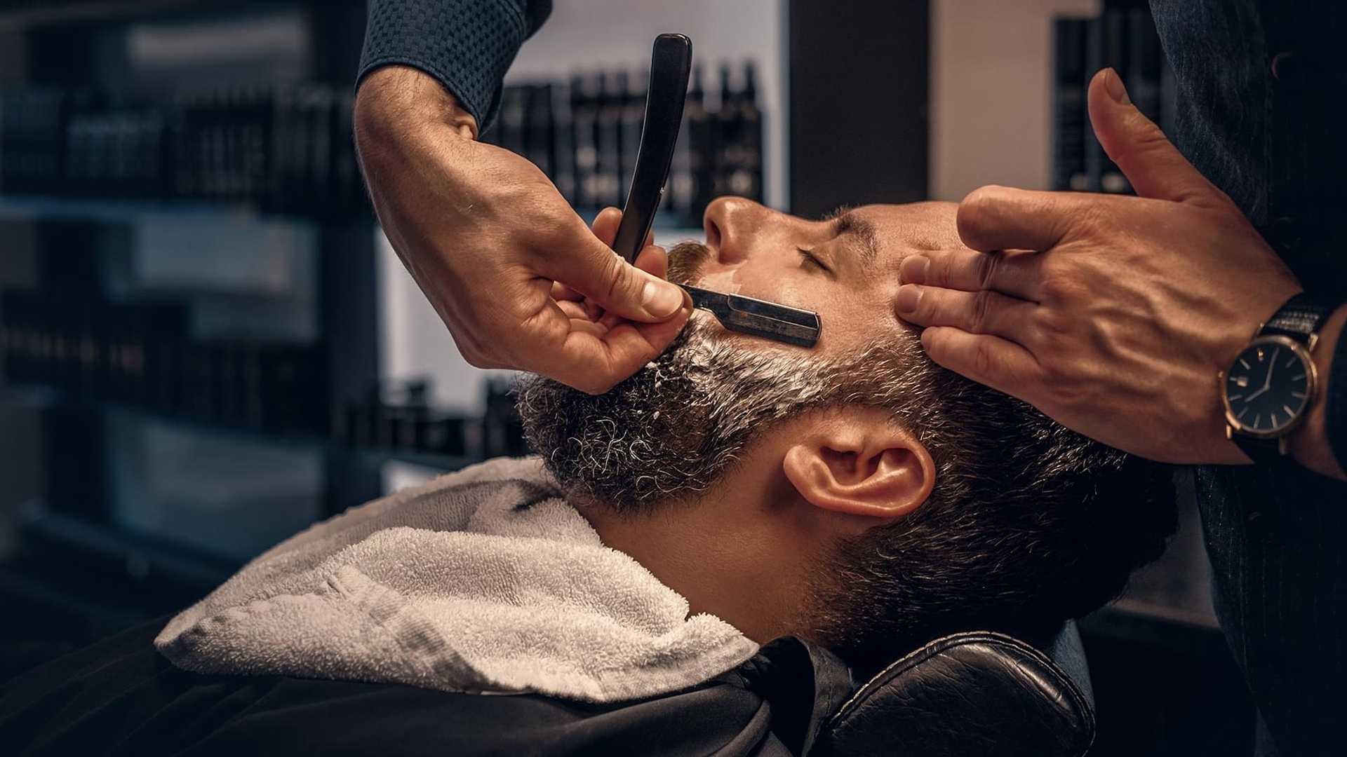 Man receiving a shave at a barbershop, towel around neck, barber using a straight razor.