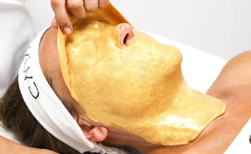Person receiving a luxurious gold facial treatment at a spa.