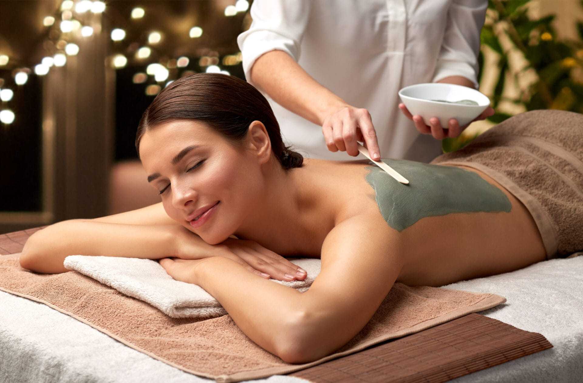 Woman enjoying a relaxing back spa treatment with green clay mask being applied.