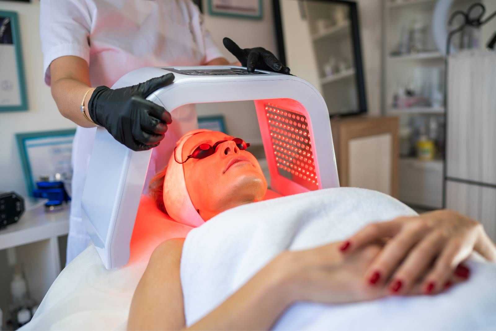 Woman undergoing LED light therapy facial treatment at a clinic.