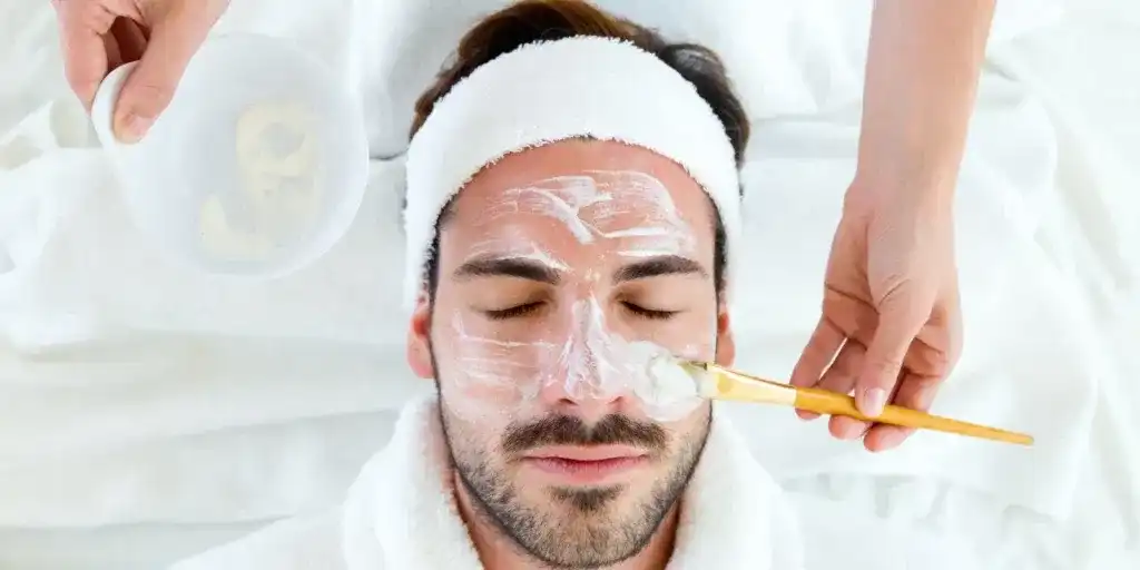 Man receiving a facial treatment. Face mask applied with a brush. Relaxing spa session.