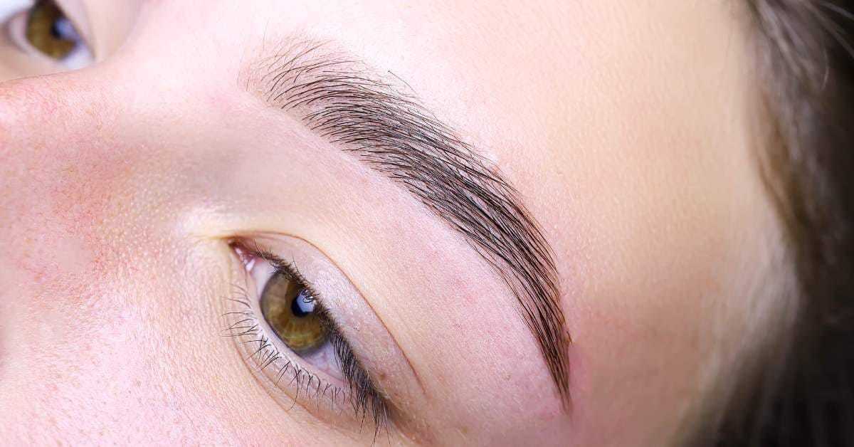 Close-up of a well-groomed eyebrow on a person's face with light brown eyes.
