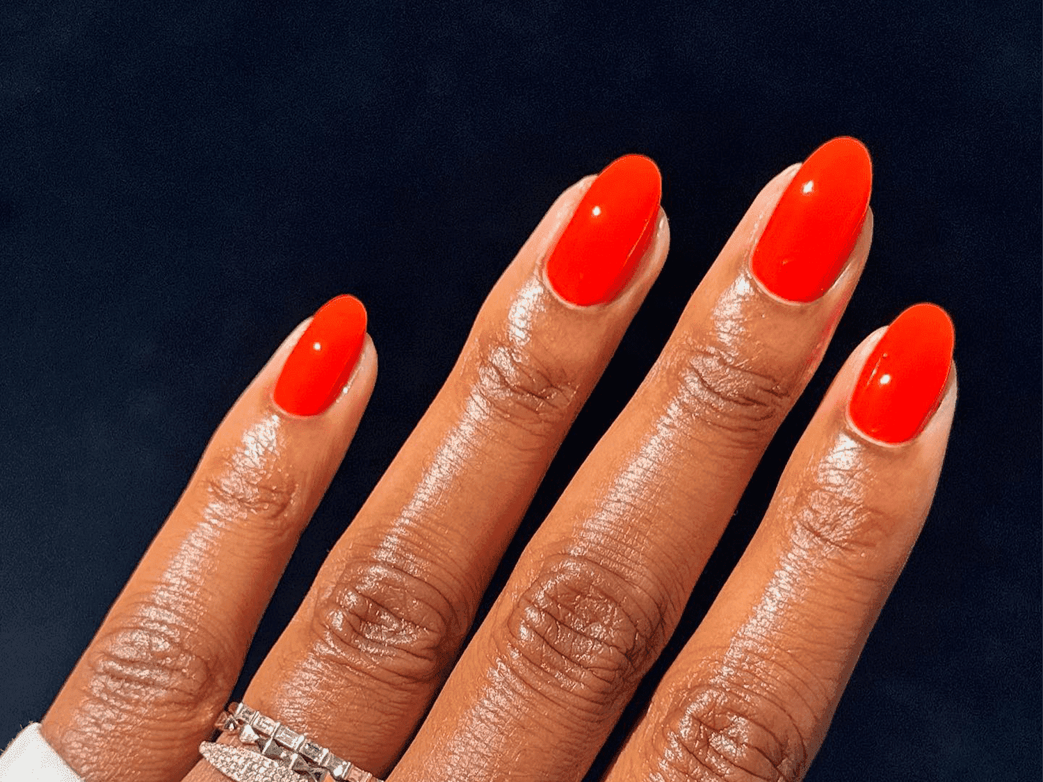 Bright orange manicure on a person's fingernails against a dark background.