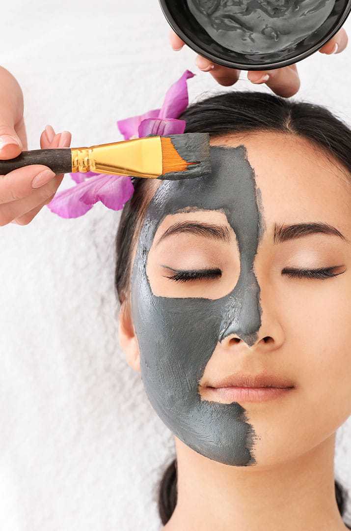 Woman receiving a facial clay mask treatment at a spa.