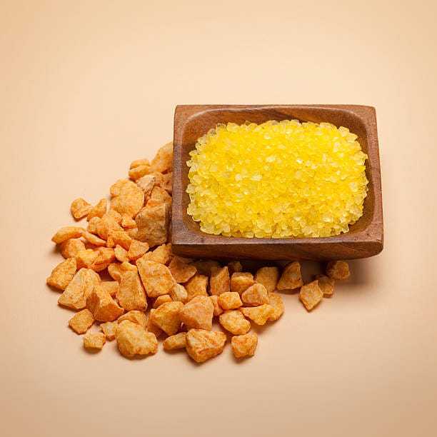 Yellow and orange resin pieces in a wooden tray on a beige background.