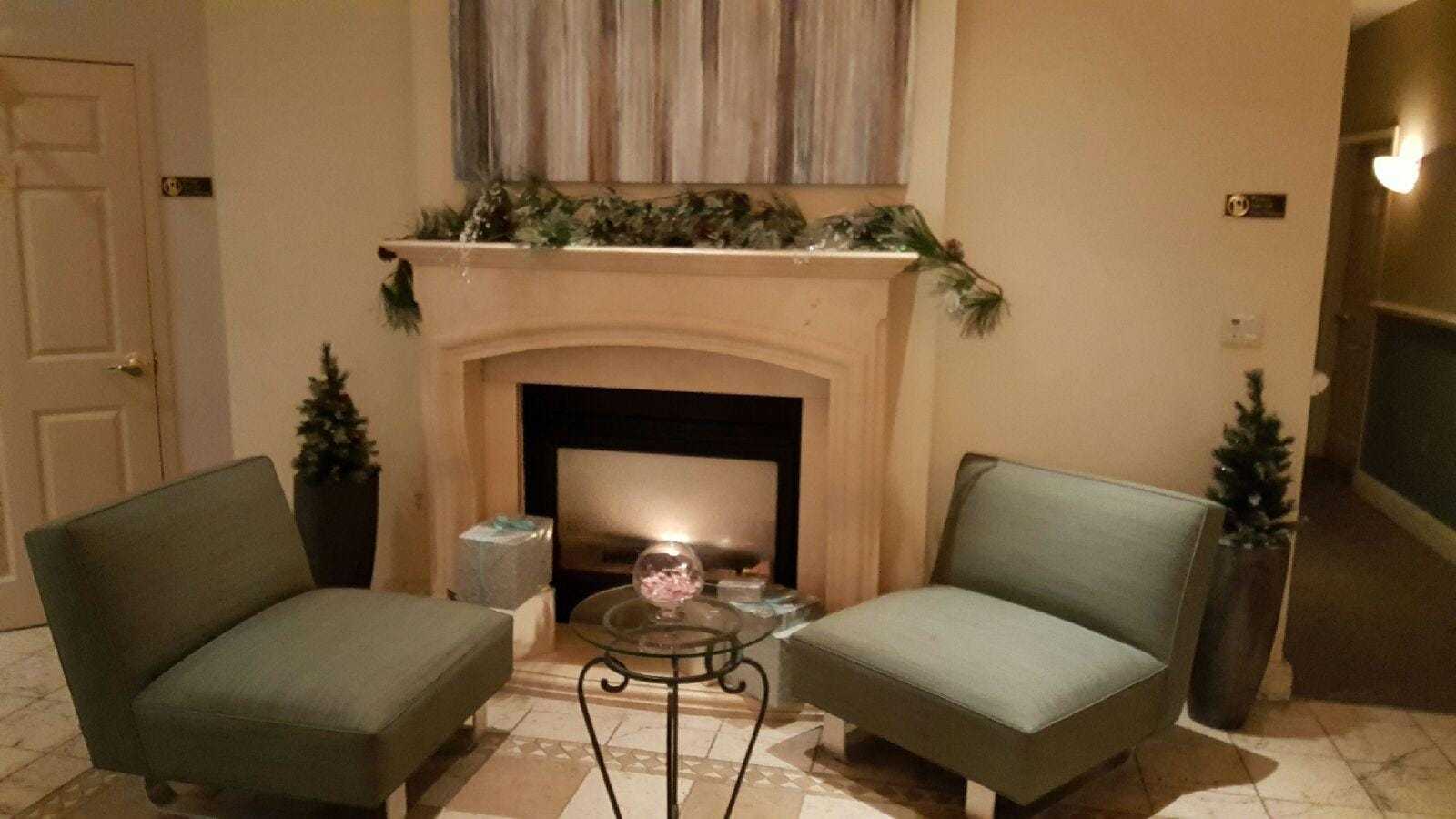 Cozy seating area with a fireplace, two chairs, a table, and festive decorations.