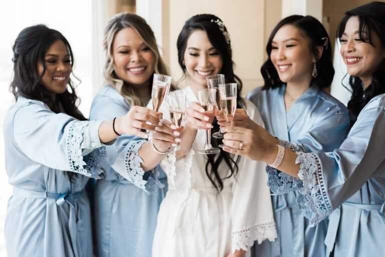 Bridesmaids in blue robes toasting with champagne, celebrating the bride in white.