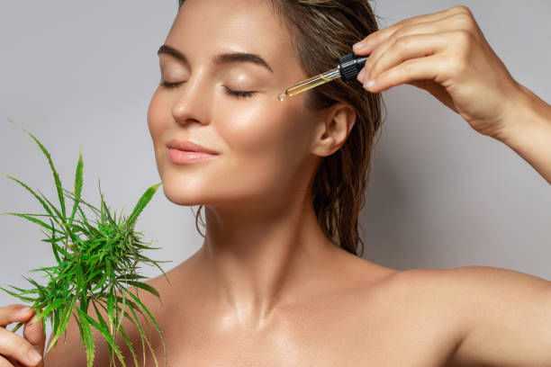Skin care with hemp: Woman applies oil to face, holding hemp leaf.