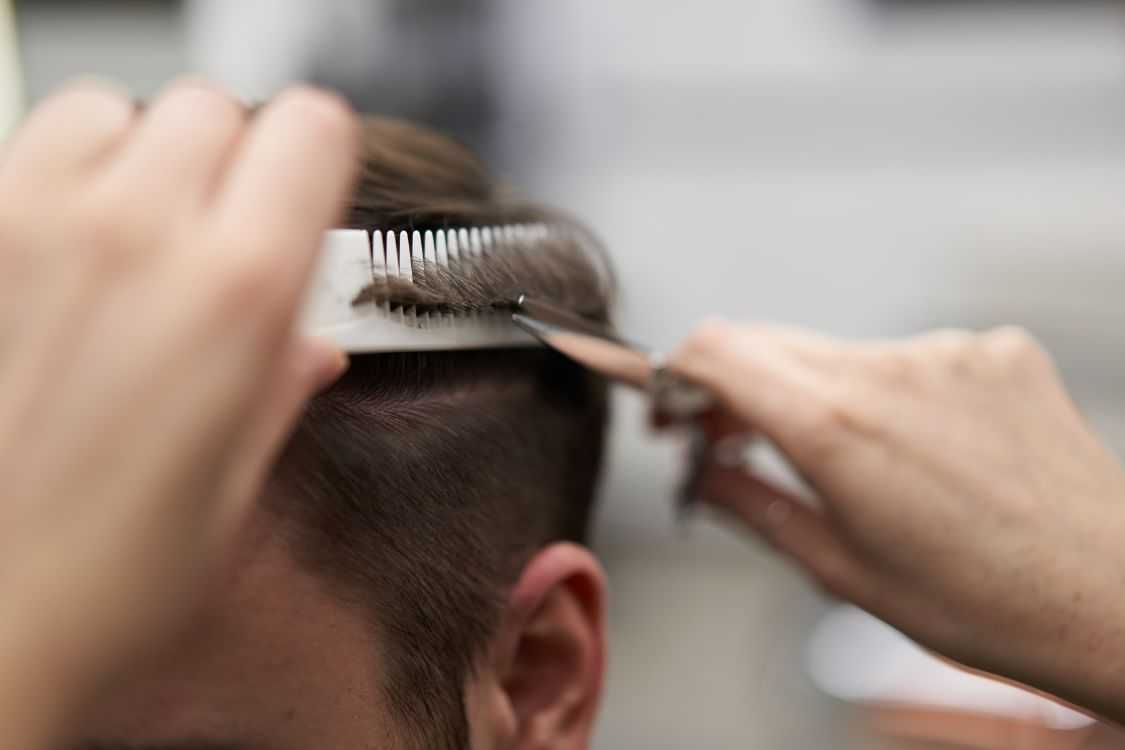 Close-up of a person getting a haircut with scissors and comb in a salon.