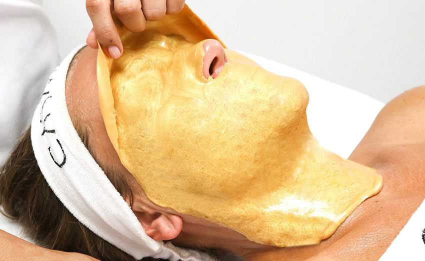 Person receiving a luxurious gold facial treatment at a spa.