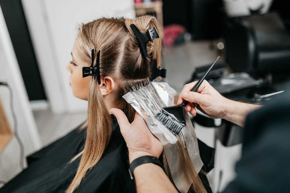 Hairdresser applying dye to client's hair at salon.
