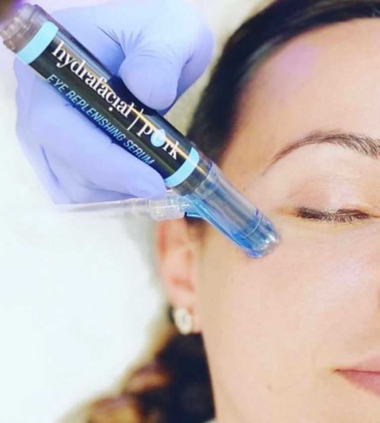 Aesthetician applying HydraFacial Perk eye serum to a woman's under-eye area.
