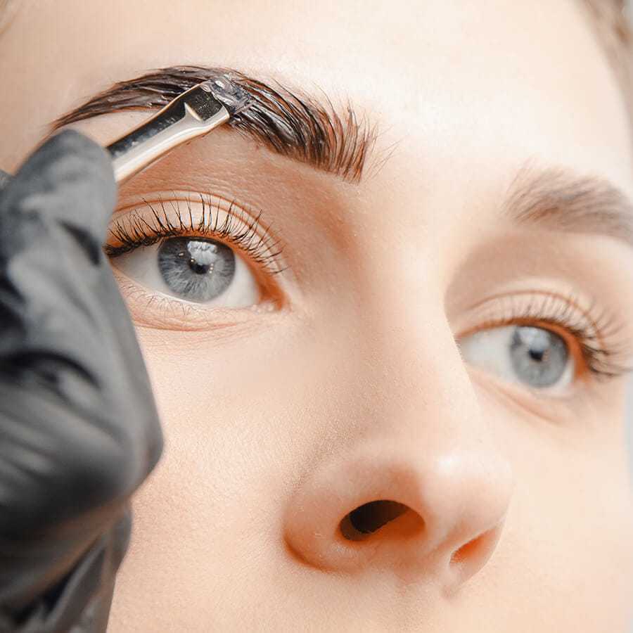 Eyebrow tinting in progress with black dye being applied using tweezers.