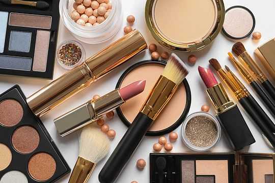 Various makeup products including brushes, lipsticks, powders, and eyeshadows in soft pink and gold tones.