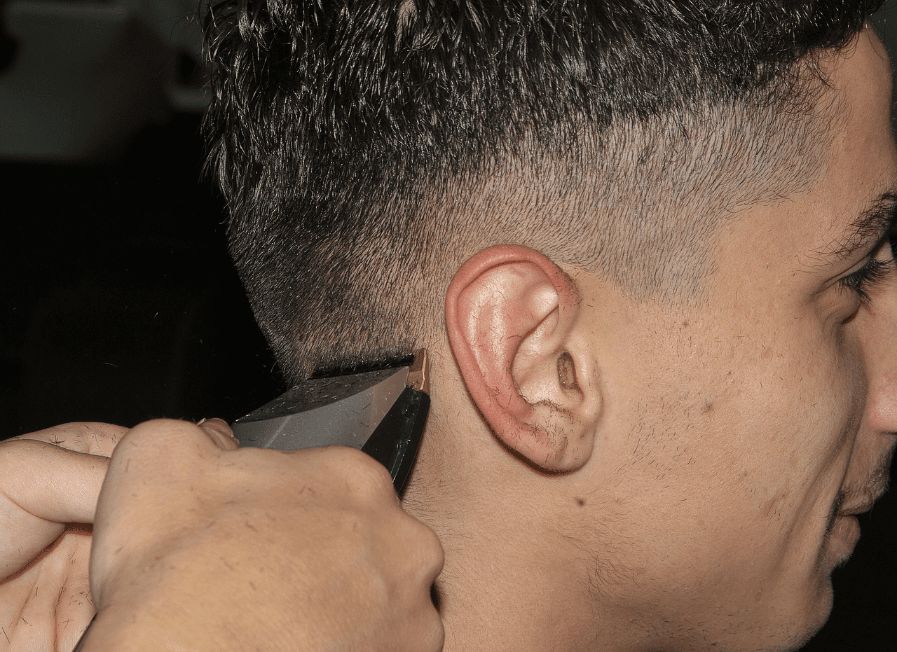 Man receives a haircut with clippers, showing close-up of hair and skin fade.