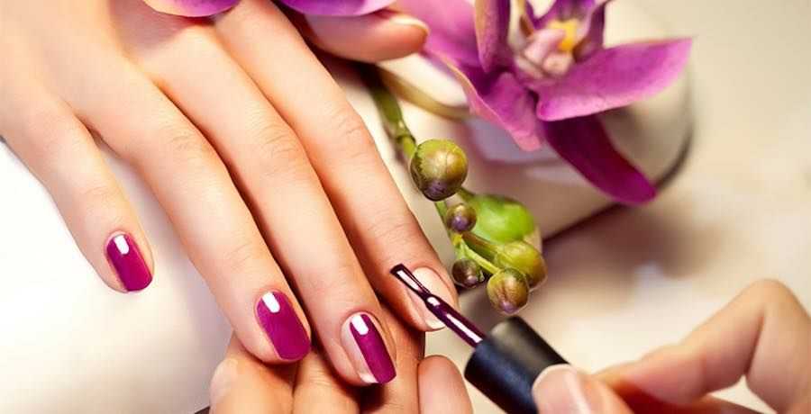 Person applying purple nail polish beside orchid flowers.