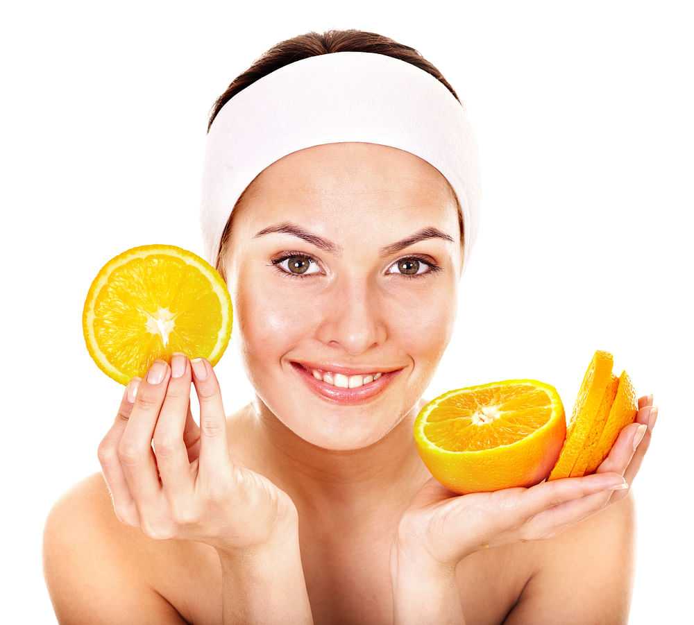 Woman smiling, holding orange slices, promoting skincare.