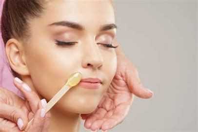 Woman receiving facial waxing with a wooden applicator on her upper lip.