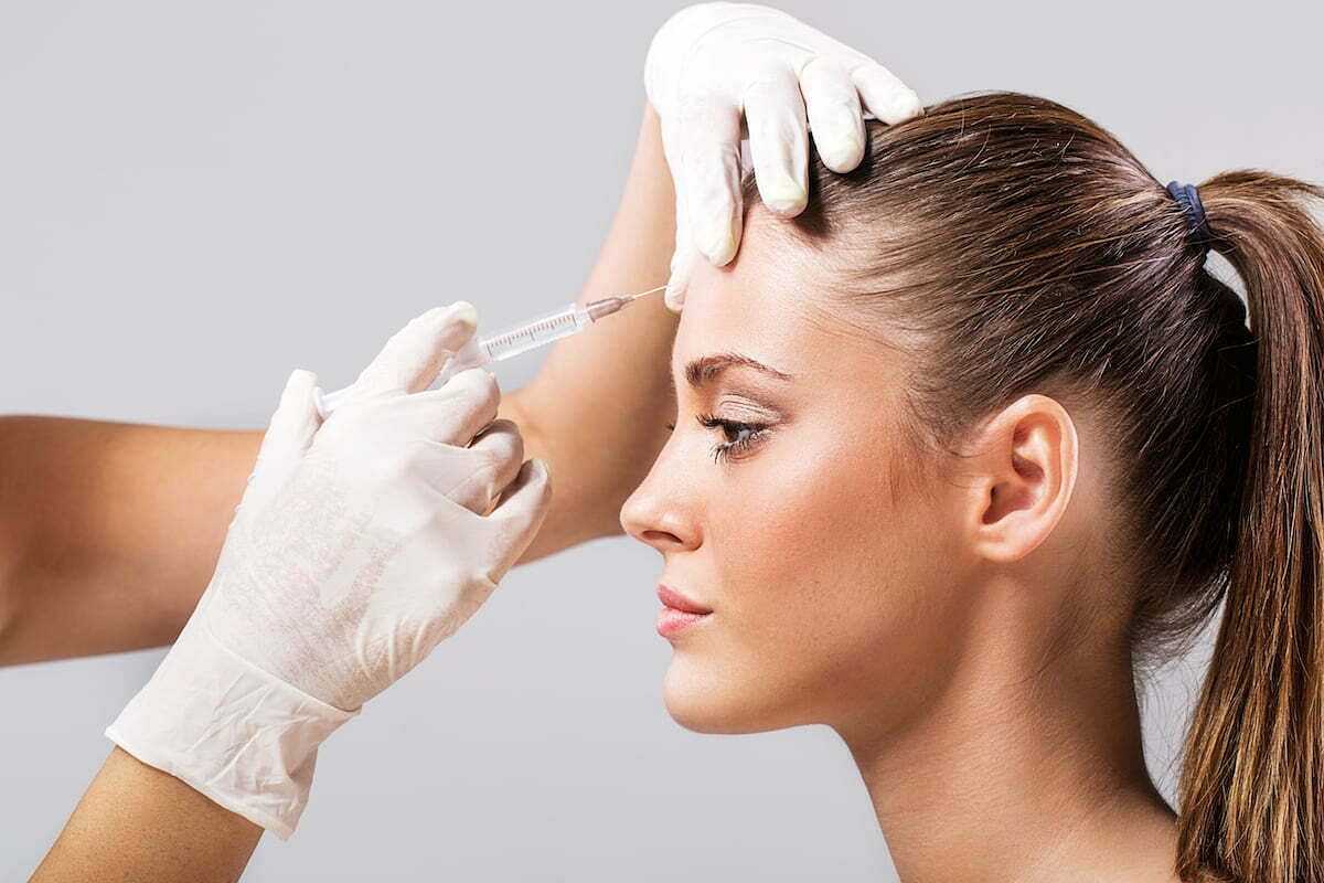 Person receiving a cosmetic injection in the forehead by a gloved practitioner.