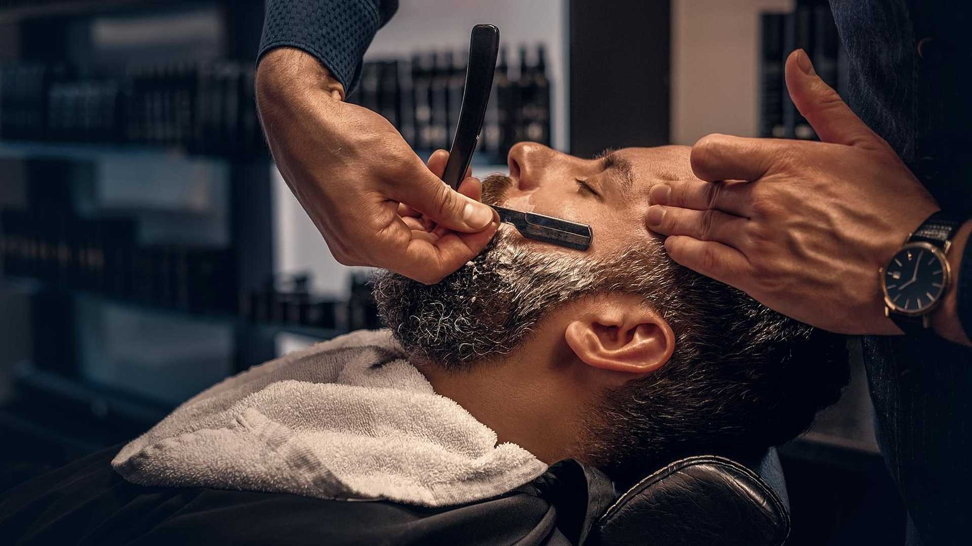 Close-up of a man receiving a traditional straight razor shave at a barbershop.