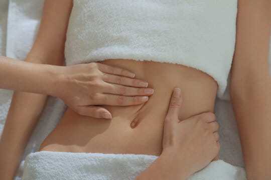 Person receiving a relaxing abdominal massage, covered with white towels.