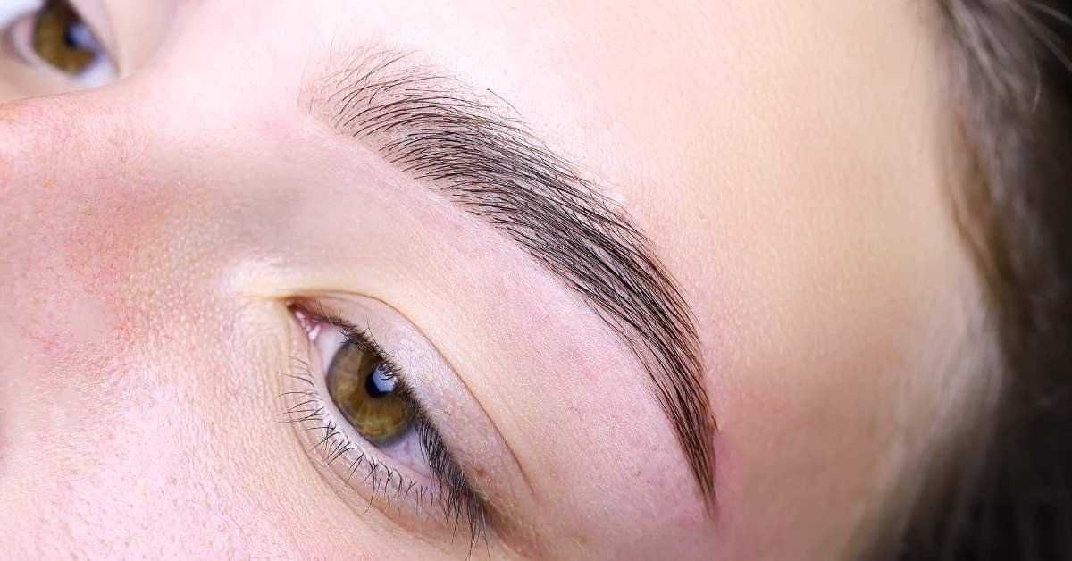 Close-up of a well-groomed eyebrow on a person's face with light brown eyes.