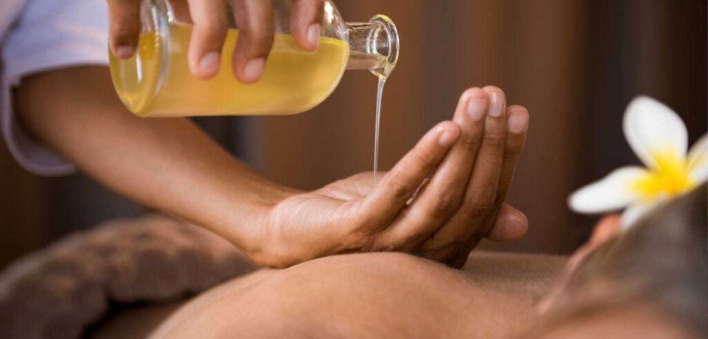 Massage oil being poured onto a person's back in a relaxing spa setting.