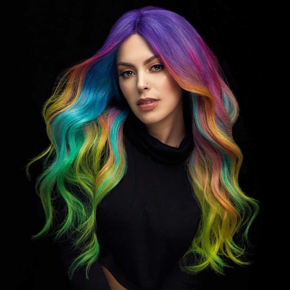 Woman with long, vibrant rainbow-colored hair against a black background.
