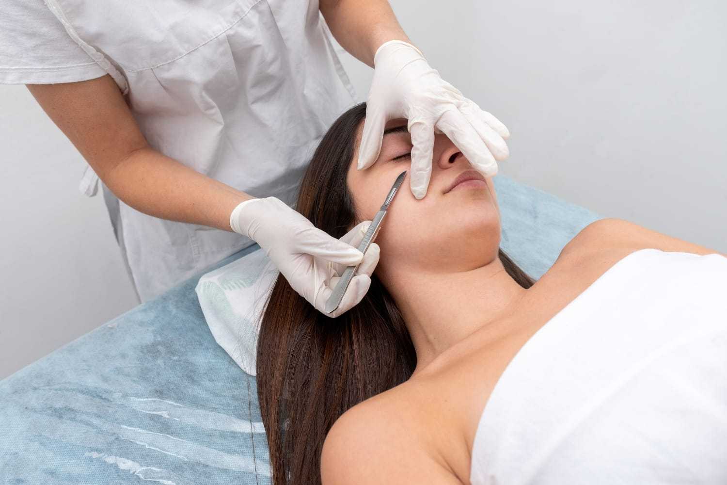 Aesthetician performing a facial treatment on a reclining woman.