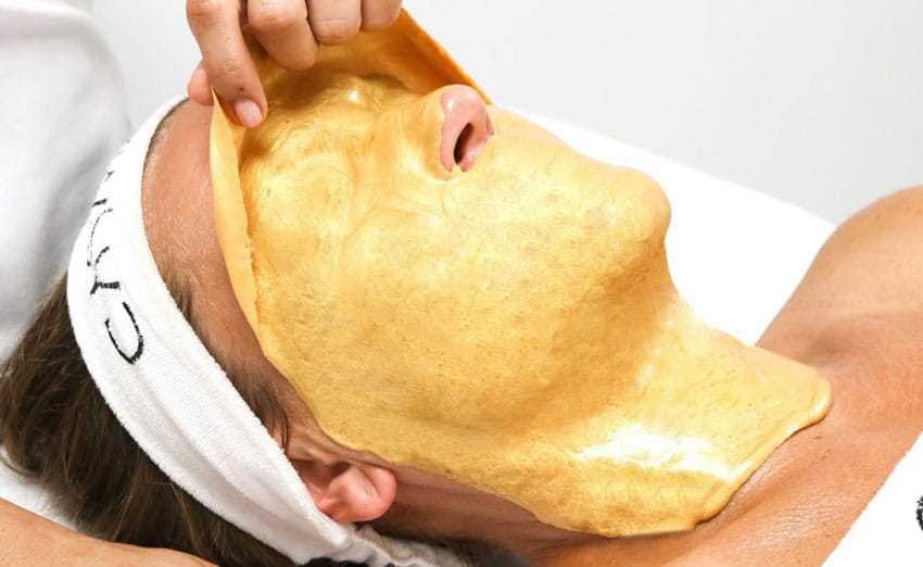 Person receiving a luxurious gold facial treatment at a spa.