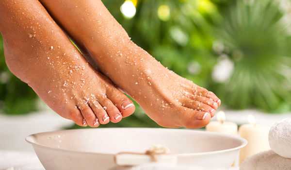 Close-up of feet with salt above a soaking bowl, spa setting.
