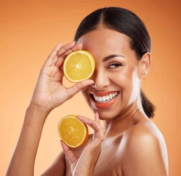 Smiling woman holding orange slices against an orange background.