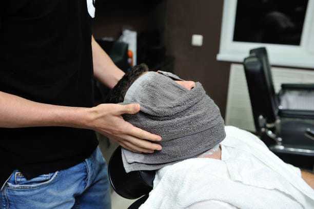 Man receiving a hot towel treatment at a barbershop.