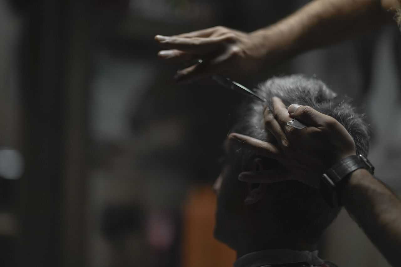 Man getting a haircut with scissors in a dimly lit barbershop.