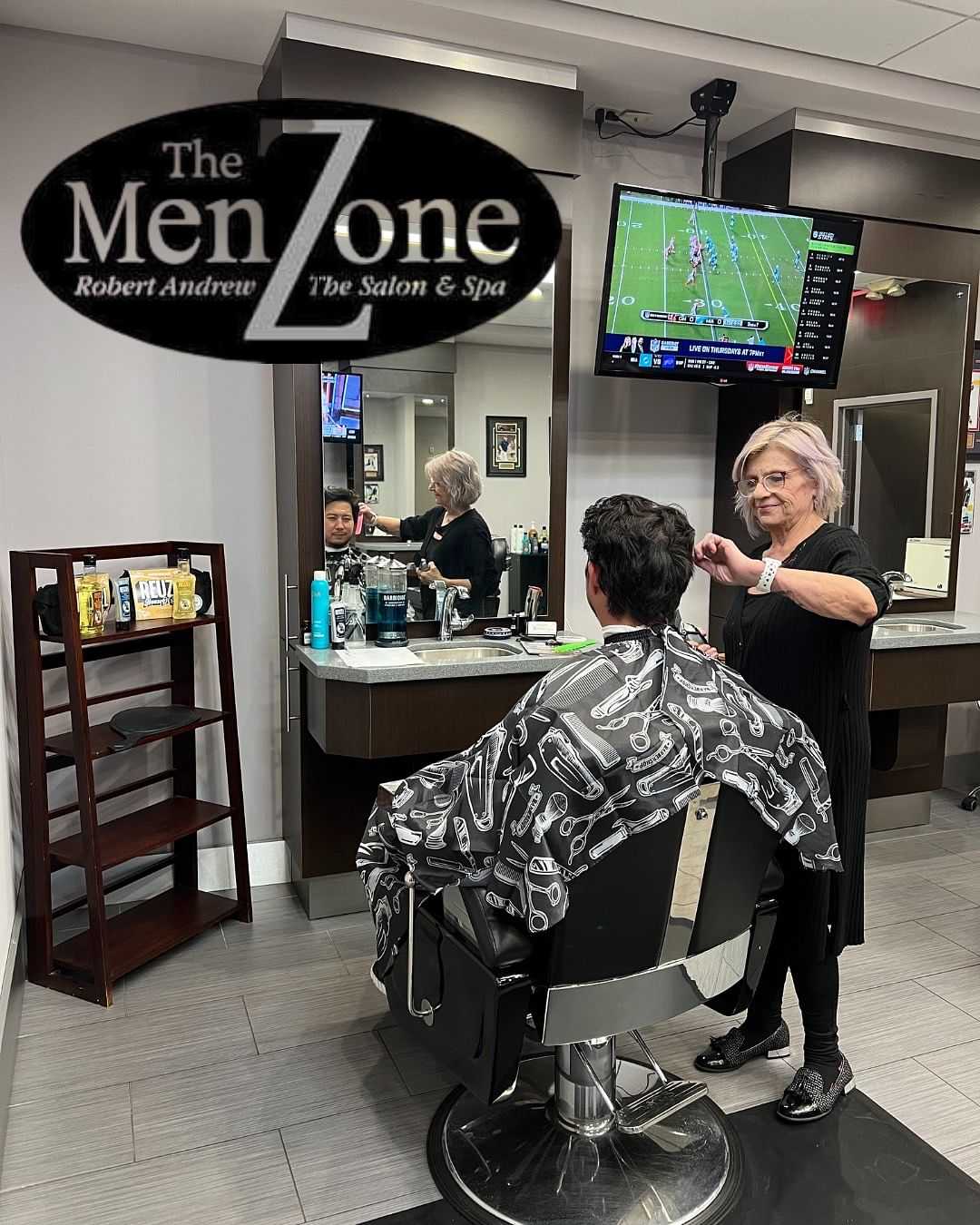 Man getting haircut at The Men Zone salon with sports on TV.