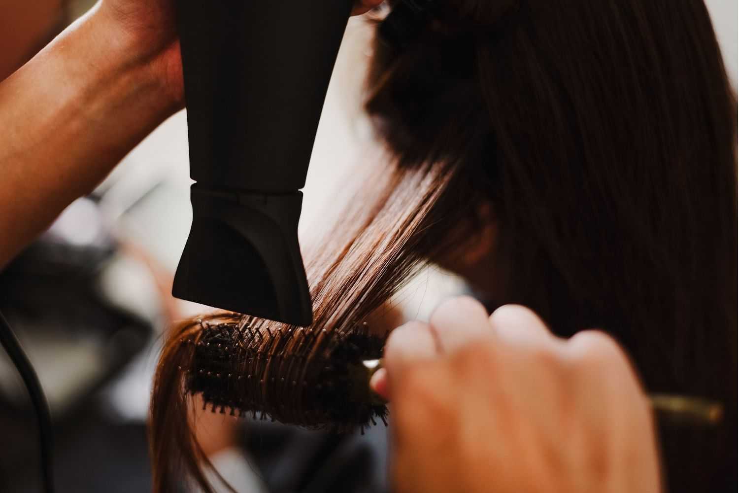 Hairdresser blow-drying and styling brown hair with a round brush.